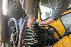 worker repairing hydraulic hoses as part of excavator maintenance